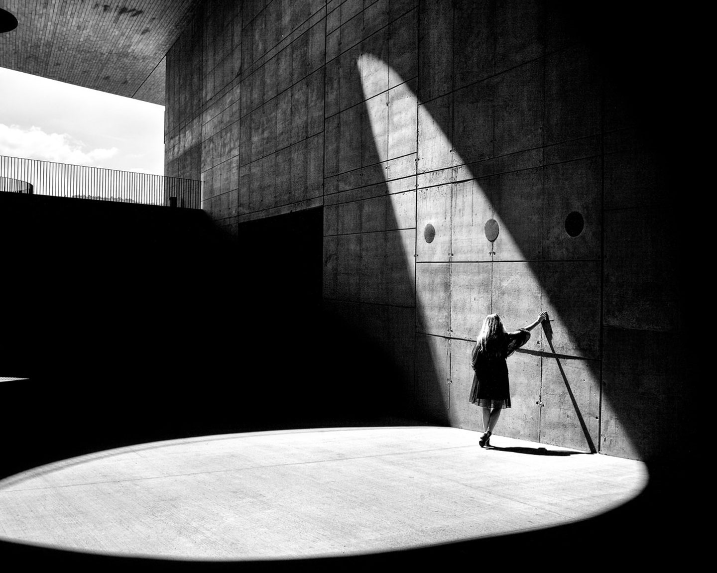 Woman standing in natural light beaming into a dark building touching a wall, taken by Allen Schaller