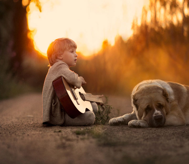 Little boy with guitar sitting on the ground with a large droopy dog
