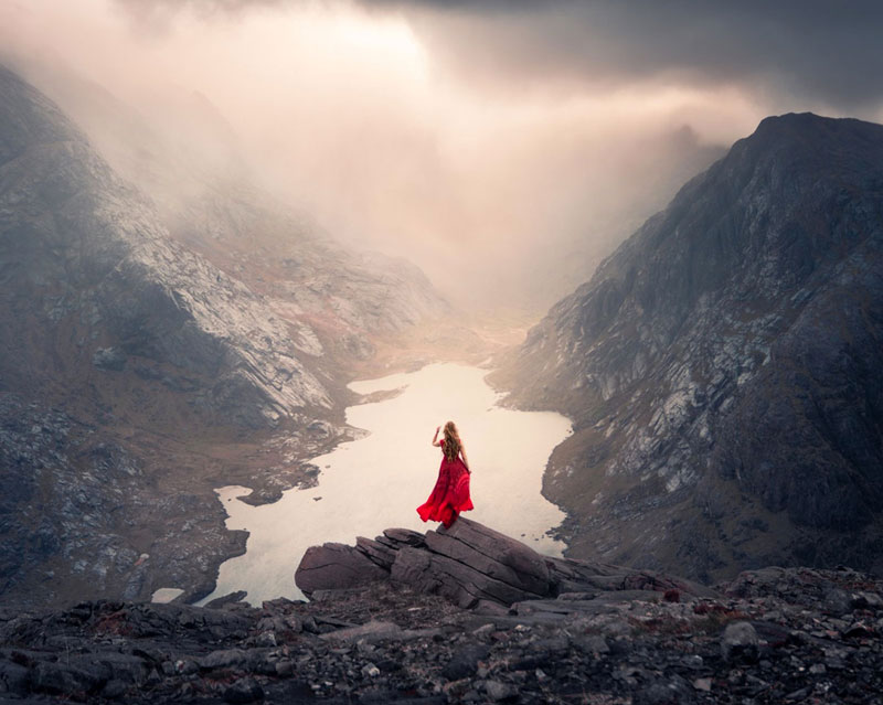 Elizabeth Gadd looks out at majestic water and mountains in Iceland in a long red dress