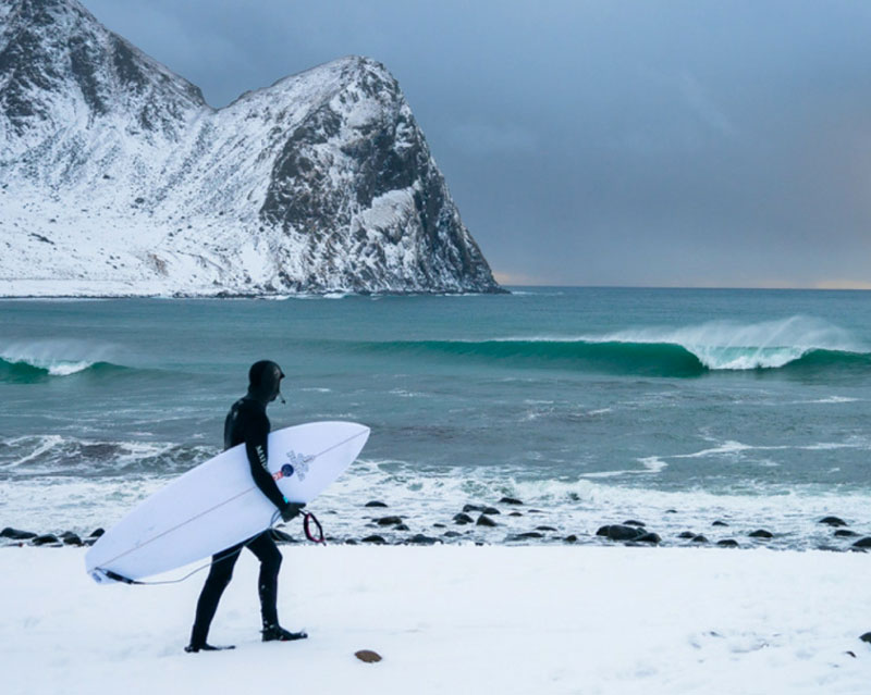 Chad Koneg walks with his surfboard toward the ocean in Norway