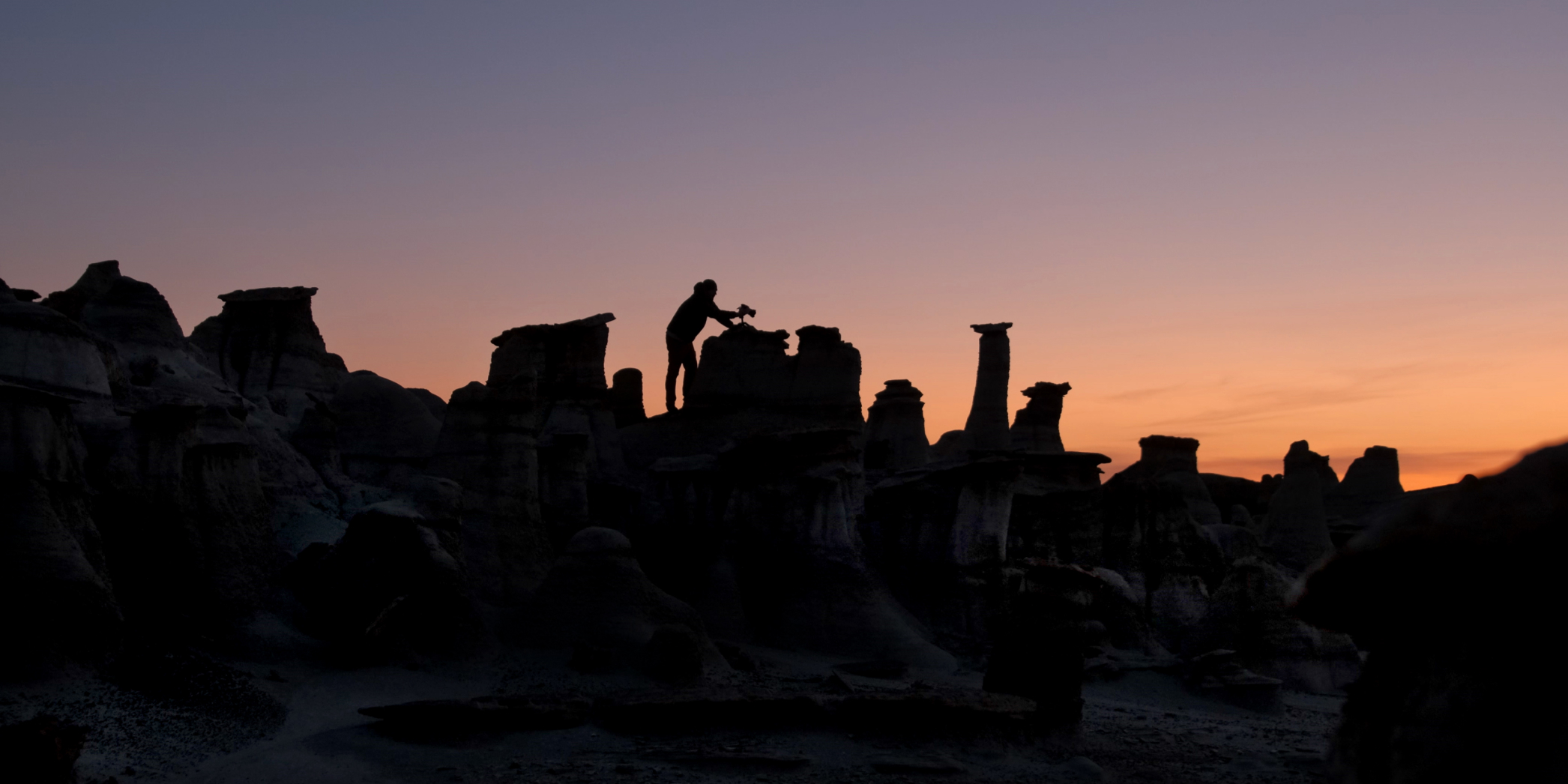 Silhouette of photographer Andy Best leaning over rock formations with a camera at sunset