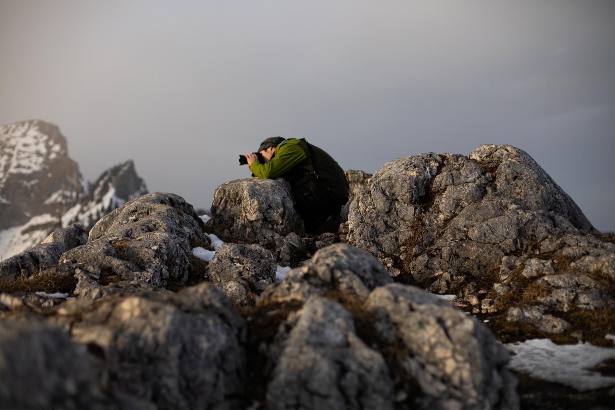 A photograph of a photographer shooting among mossy rocks, with a grey sky in the background. Photo by Benjamin Kaufmann.