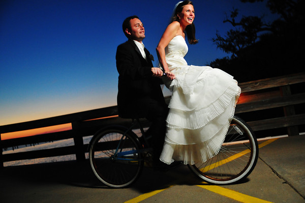 A groom riding a bicycle while his bride sits on the handlebars.