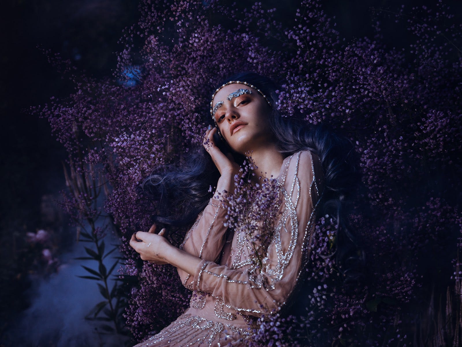 A fashionable young woman posing amid a background of lavendar flowers.
